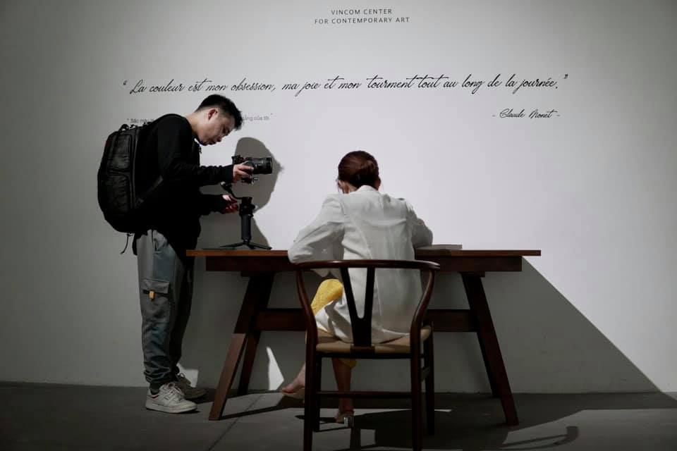Bình ngồi viết bên bàn gỗ trong gallery  khoảnh khắc soi chiếu